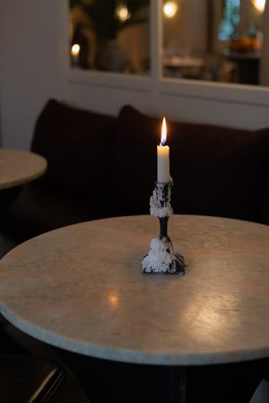Single lit candle in an ornate holder on a marble table creating a moody atmosphere.