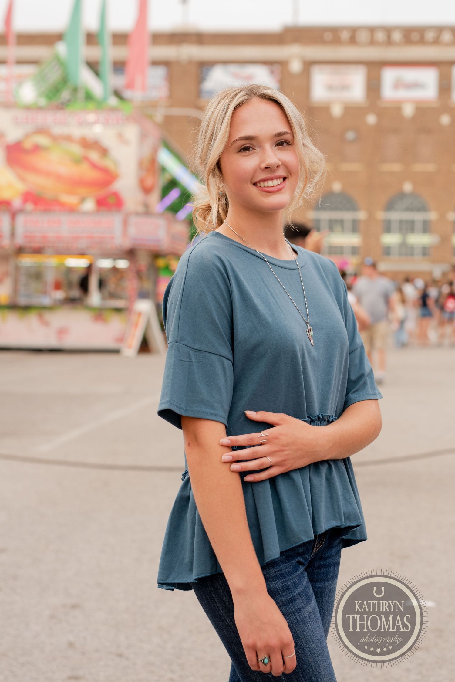 Person wearing blue peplum top at carnival with colorful rides in background.