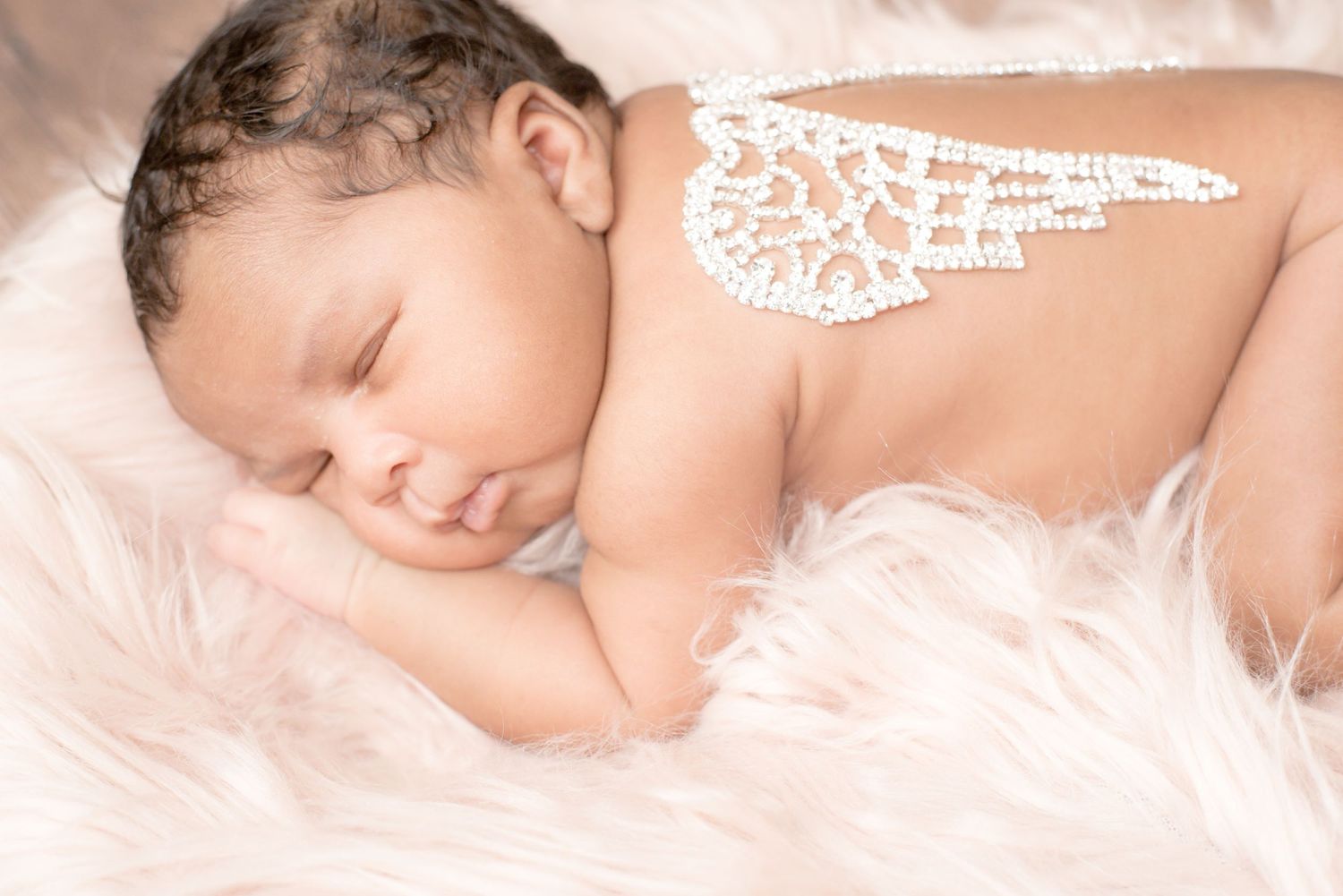 Sleeping newborn baby wearing delicate white lace wings on soft feathery bedding.