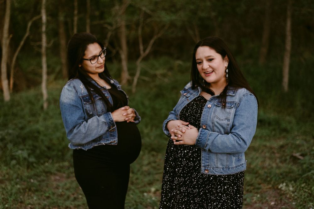 Two friends share a candid moment while wearing denim jackets in a forest setting.