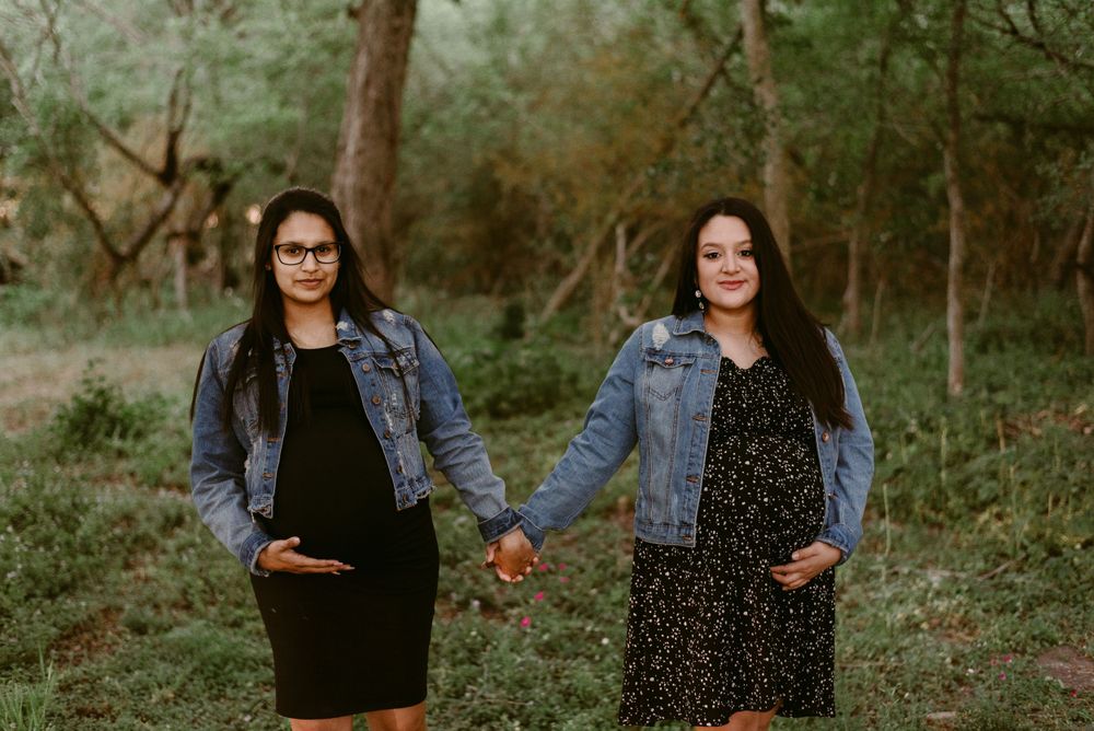 Two people wearing denim jackets hold hands while posing in a wooded area.