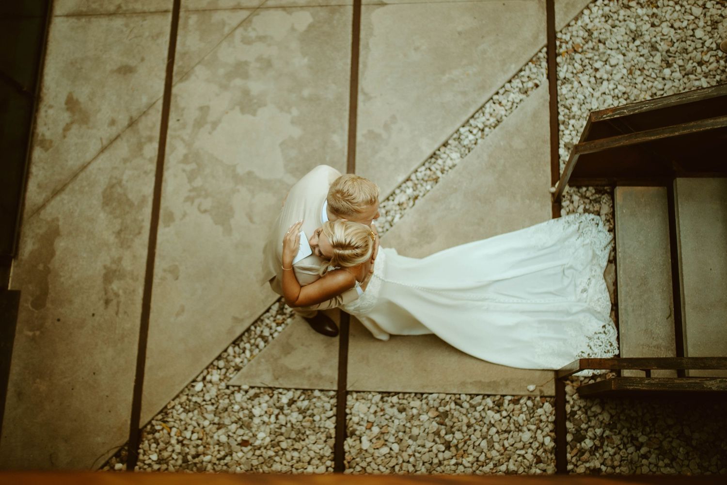 Aerial view of bride in flowing white gown and veil sitting on tiled staircase.