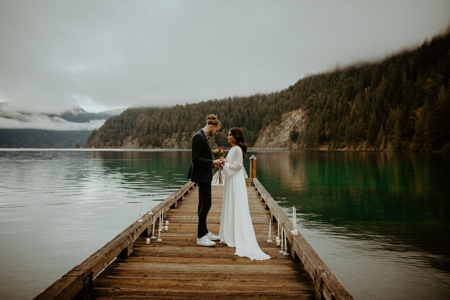 Bride and groom exchanging vows on a wooden pier with a serene mountain lake backdrop.