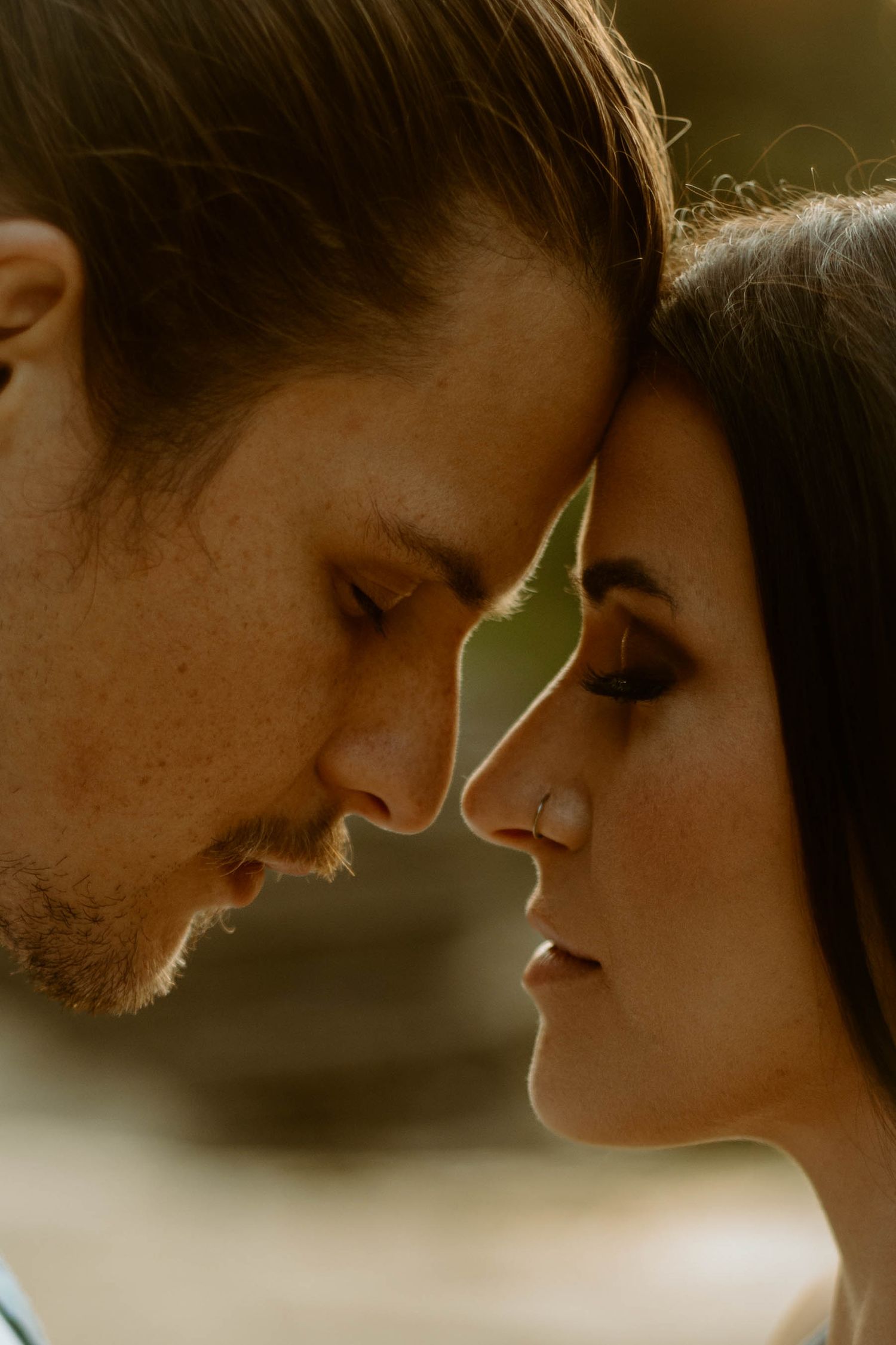 Intimate close-up portrait of couple touching foreheads with eyes closed in warm sunlight.