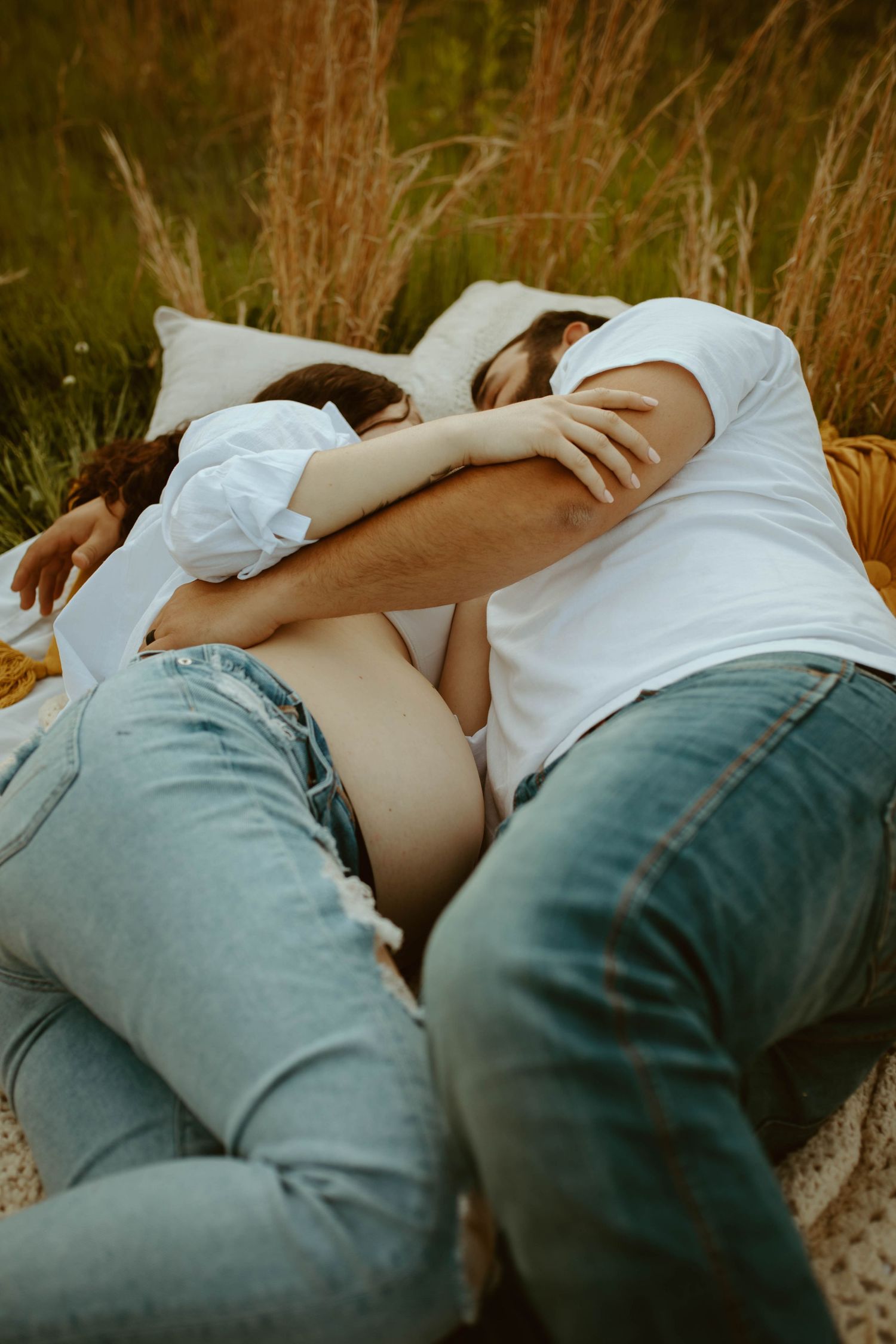 Couple lying together on a blanket in a field of tall golden grass.