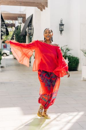 A dancer in vibrant red and orange flowing garments strikes an elegant pose in a sunlit outdoor courtyard on El Paseo in Palm Desert