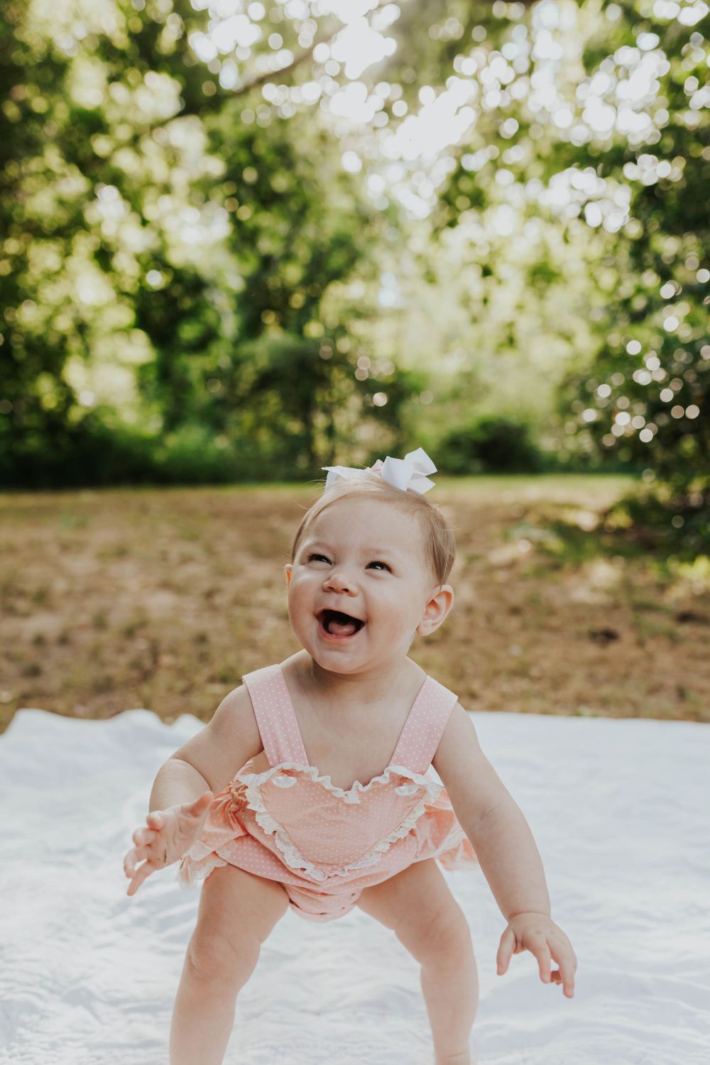 Happy baby in pink outfit showing expressions while playing on white blanket outdoors.