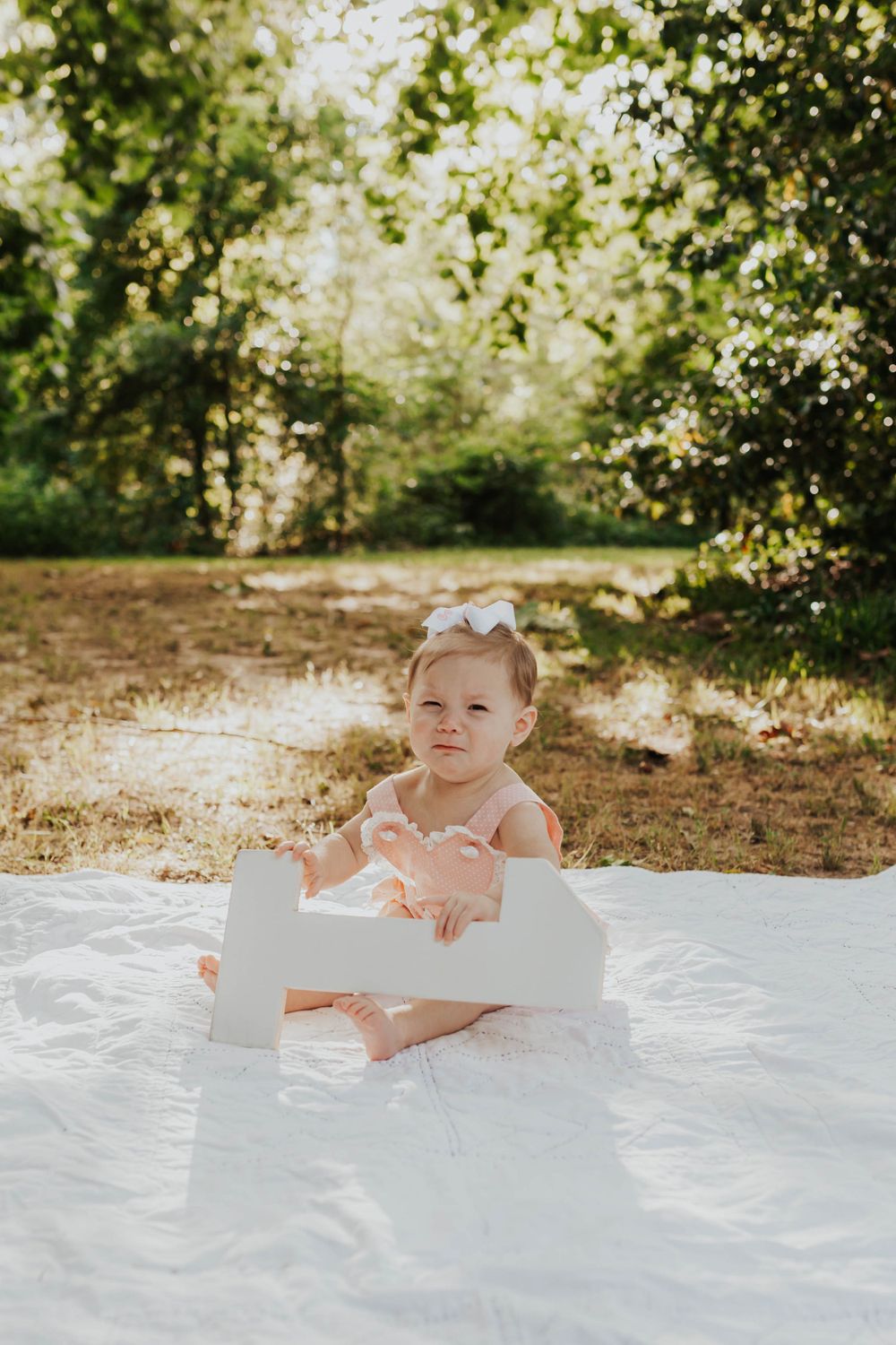 Baby in pink outfit playing on white blanket during outdoor photo session.