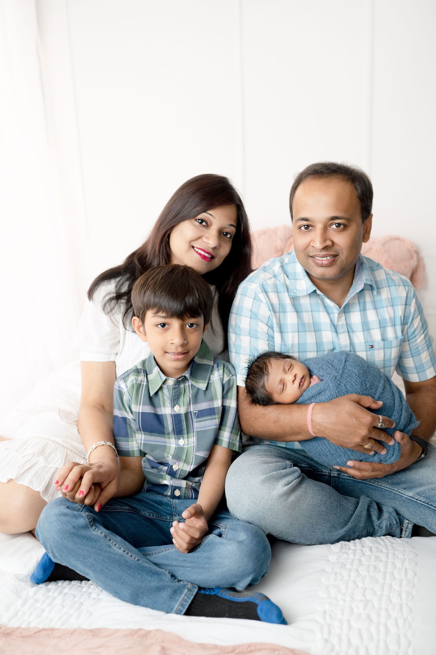 Beautiful family portrait with everyone sitting together on white bed during indoor session.