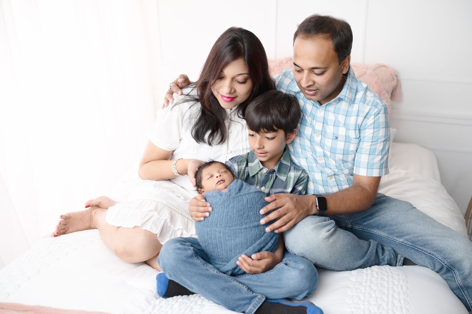 Family shares tender moment while lounging on white bedding during photo shoot.