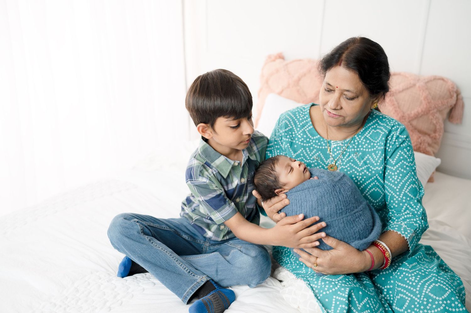 Intimate family moment captured on white bed with teal and denim clothing.