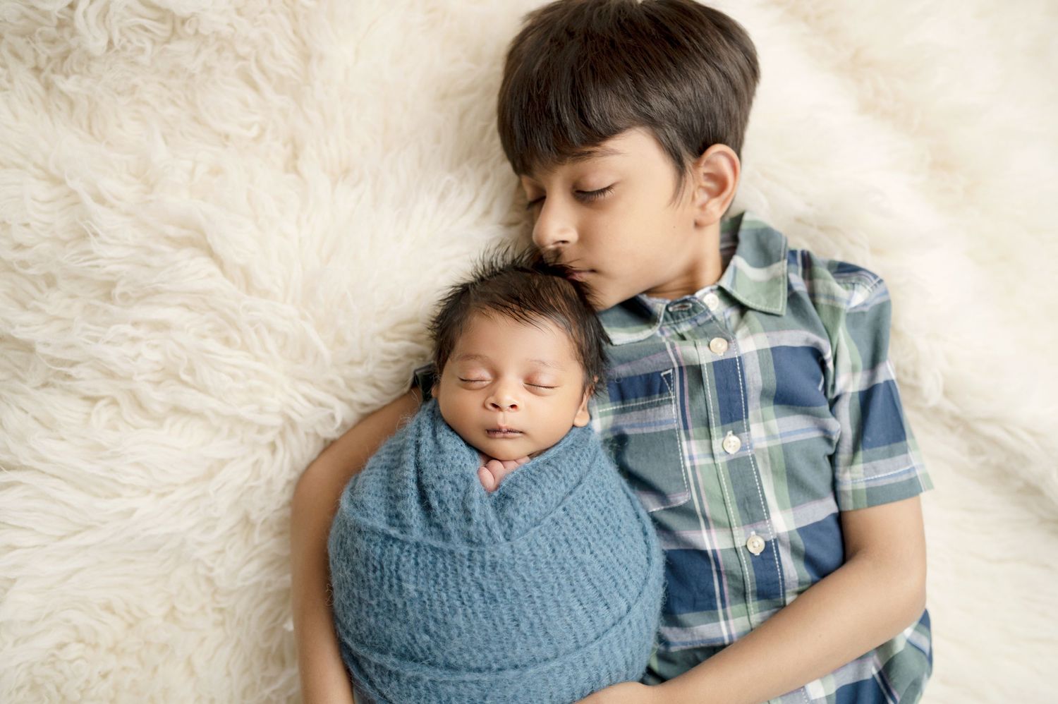 Sweet sibling moment captured on white furry rug during newborn photo session.
