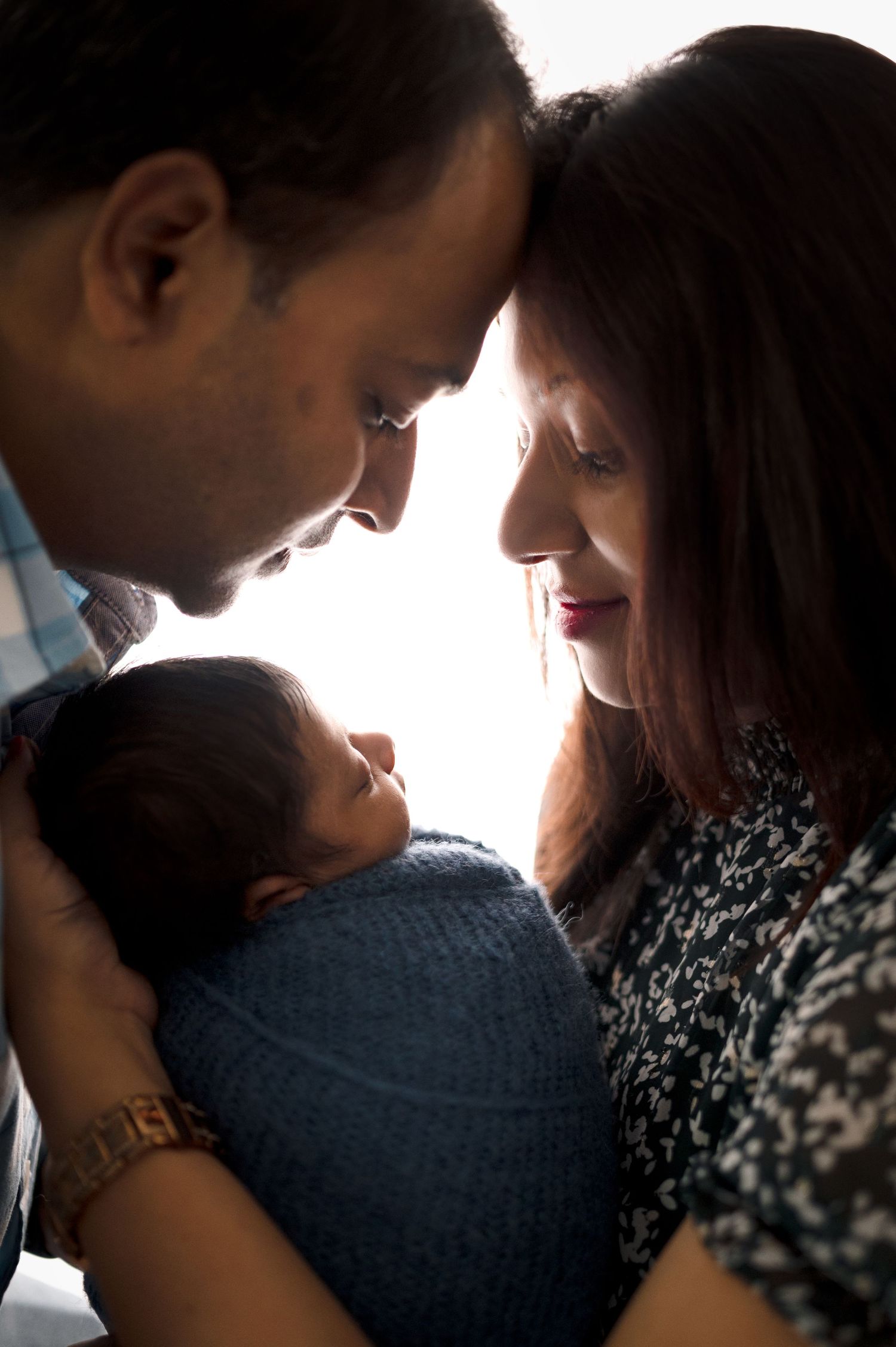 Intimate family portrait with baby in dramatic backlighting and close-up composition.