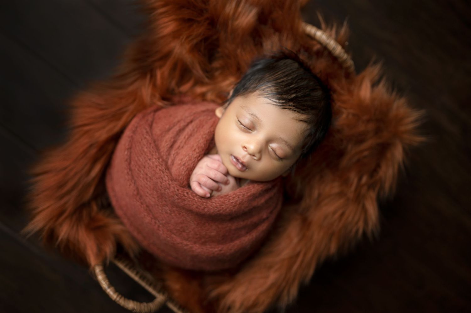Peaceful newborn sleeping soundly on brown fur blanket in professional studio photos.