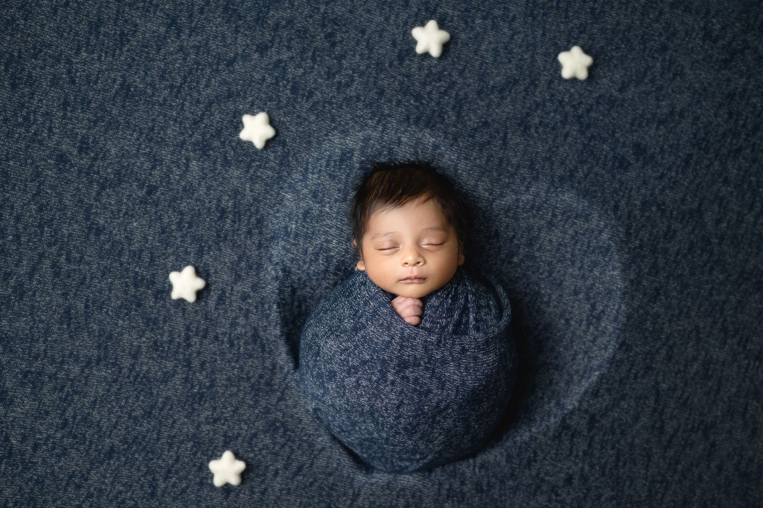 Newborn photography series with baby wrapped in blue against dark backdrop with white star decorations.