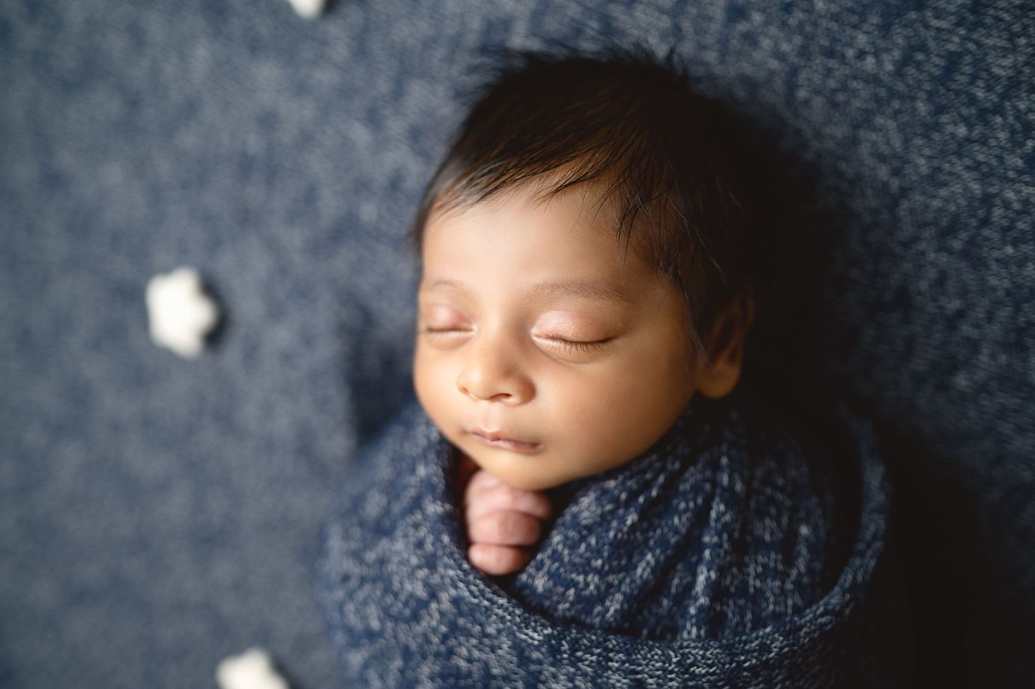 Artful newborn portraits showing sleeping baby in navy wrap against textured blue background.