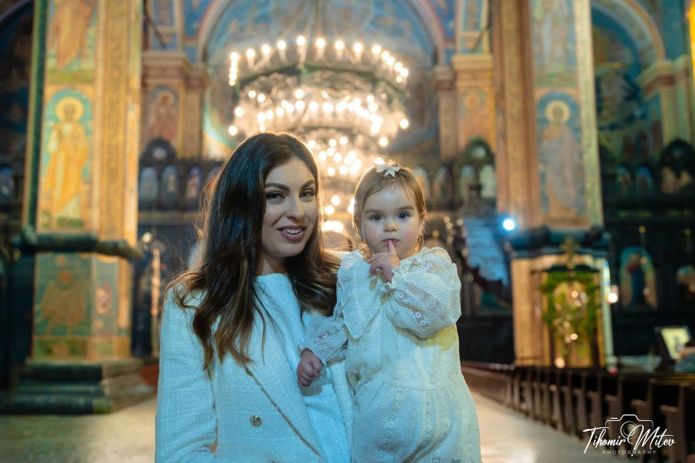 Майка и кръстено момиченце в голяма църква пред огромен полилей в Катедралата във Варна