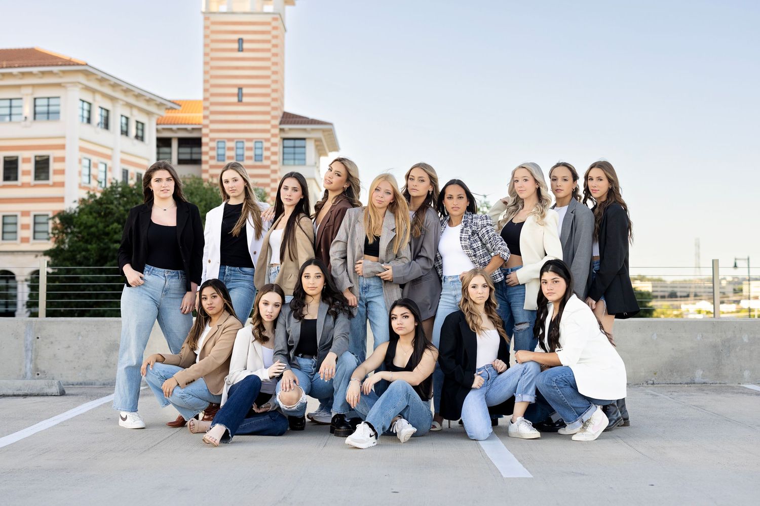 A group of casually dressed college students pose together on a rooftop with a building in the background.