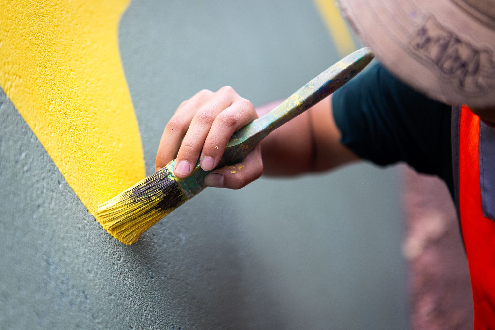 Close up photo of a person adding yellow paint to a mural with a paint brush