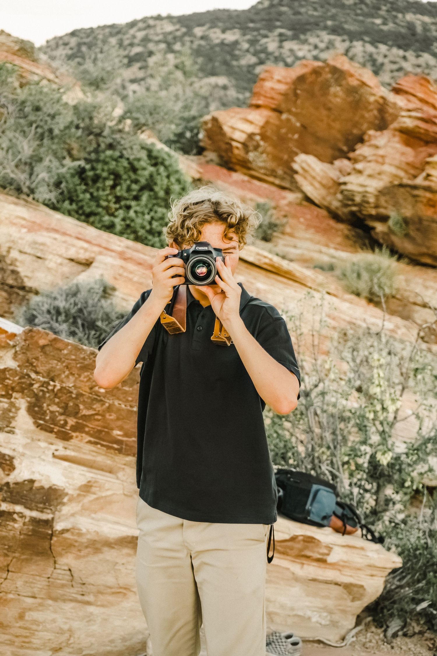 Photographer holding a vintage camera against red rock formations in a desert landscape.
