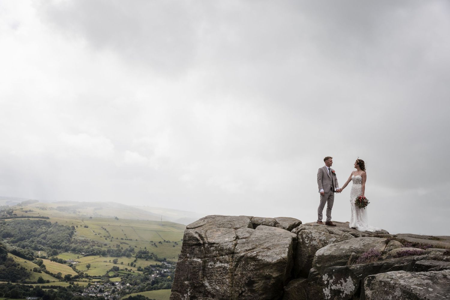 A couple stands together on a rocky mountain overlook during a misty overcast day.