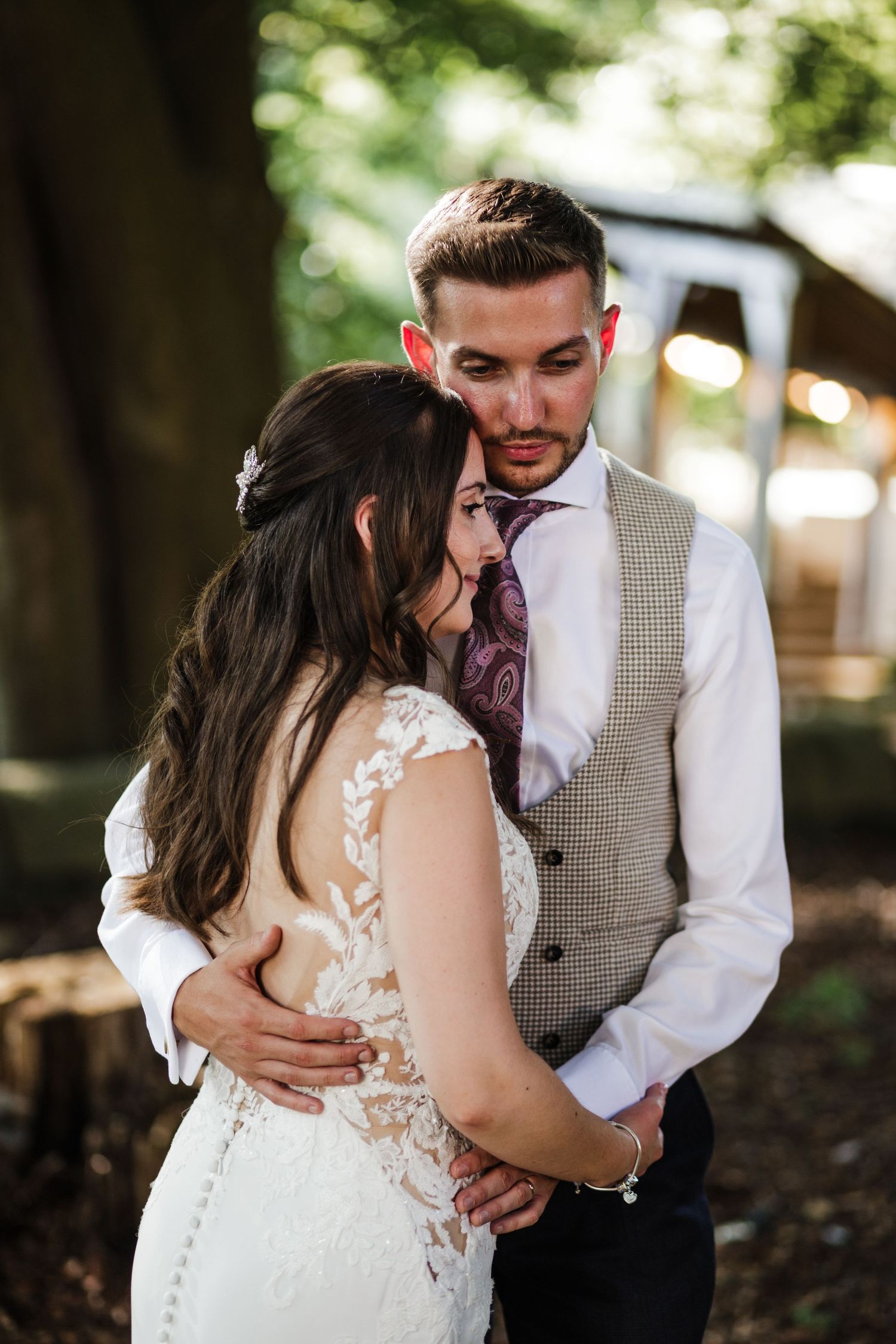 A bride and groom share intimate embraces in a romantic outdoor wedding photoshoot beneath trees with soft lighting.