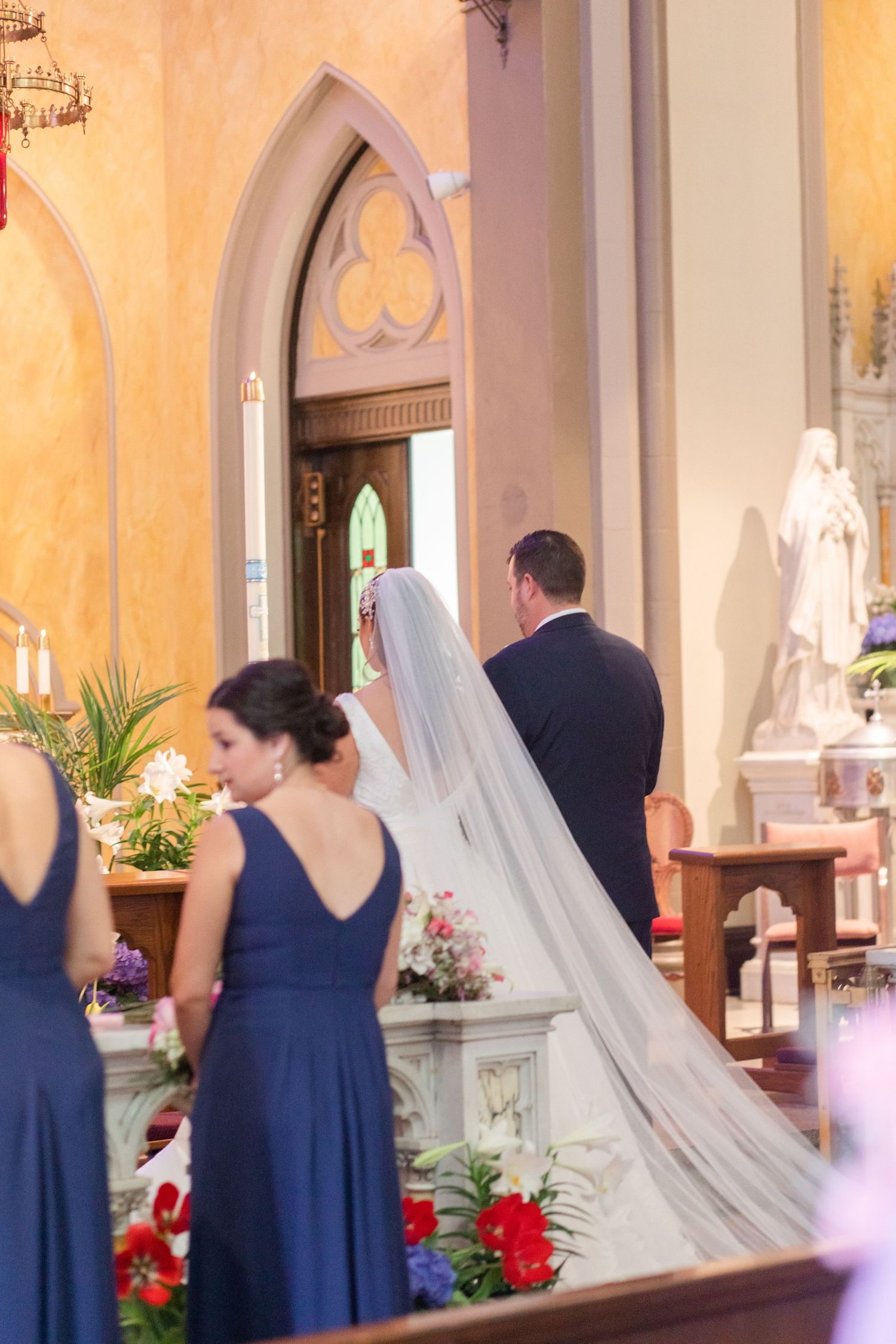 Wedding ceremony in progress at a Gothic cathedral with blue-clad attendants and white floral decorations.