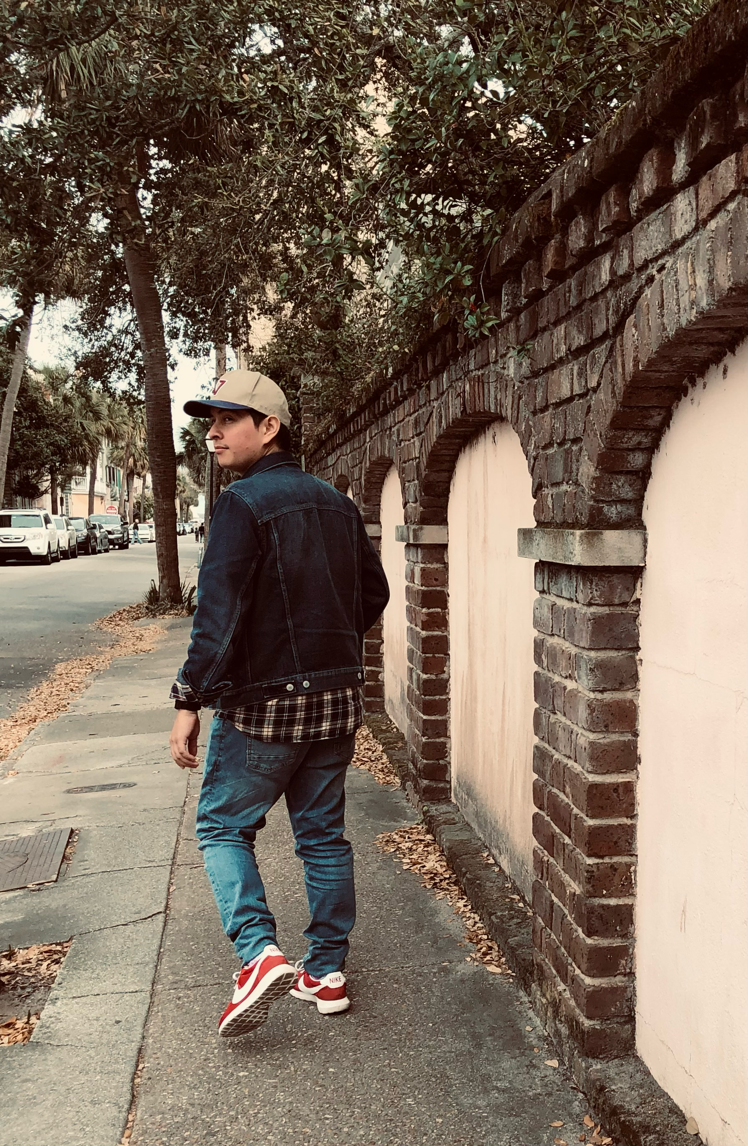 Person in casual wear walking past brick archway on urban sidewalk.