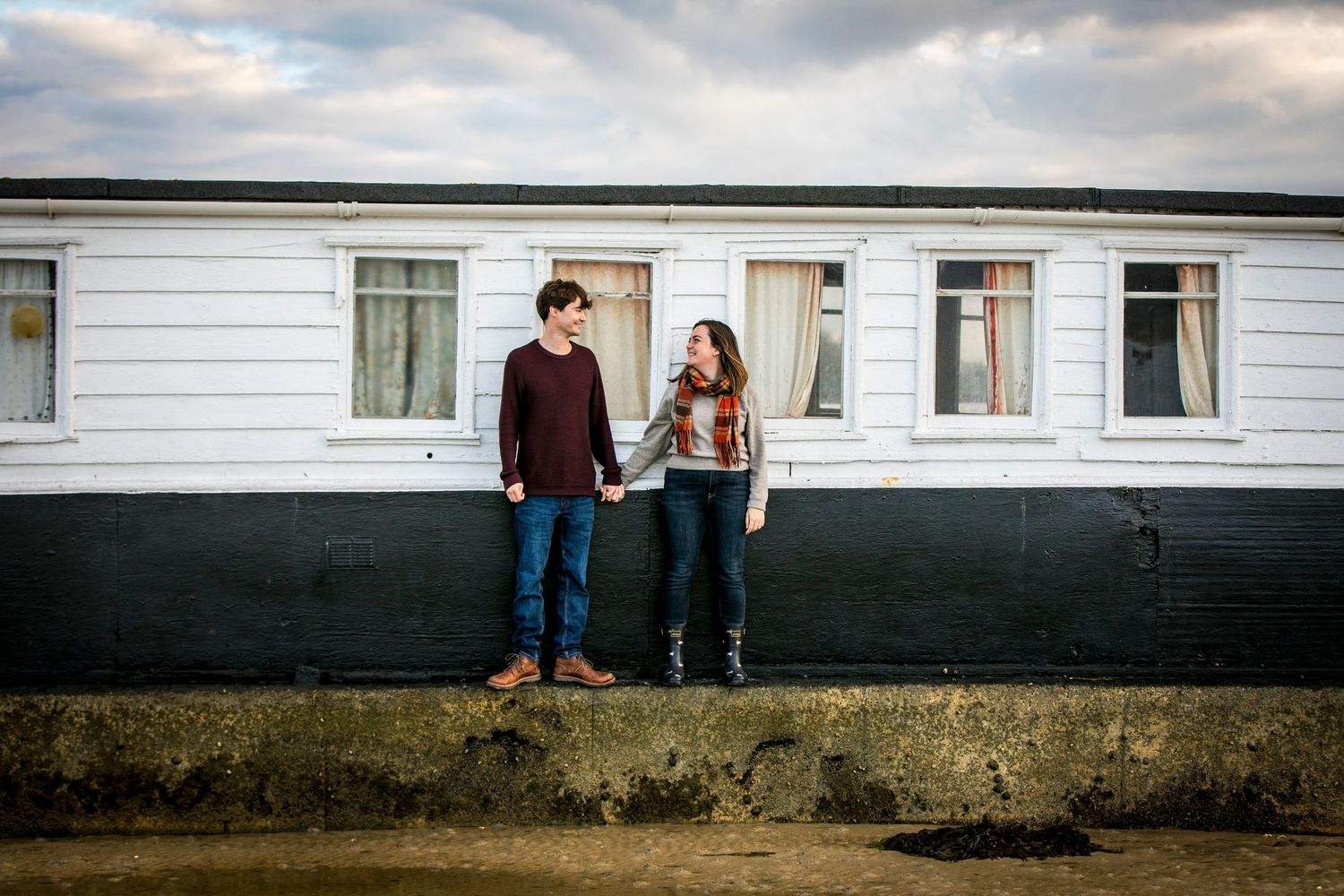 A couple stands in front of a white building exterior during an outdoor photo session.