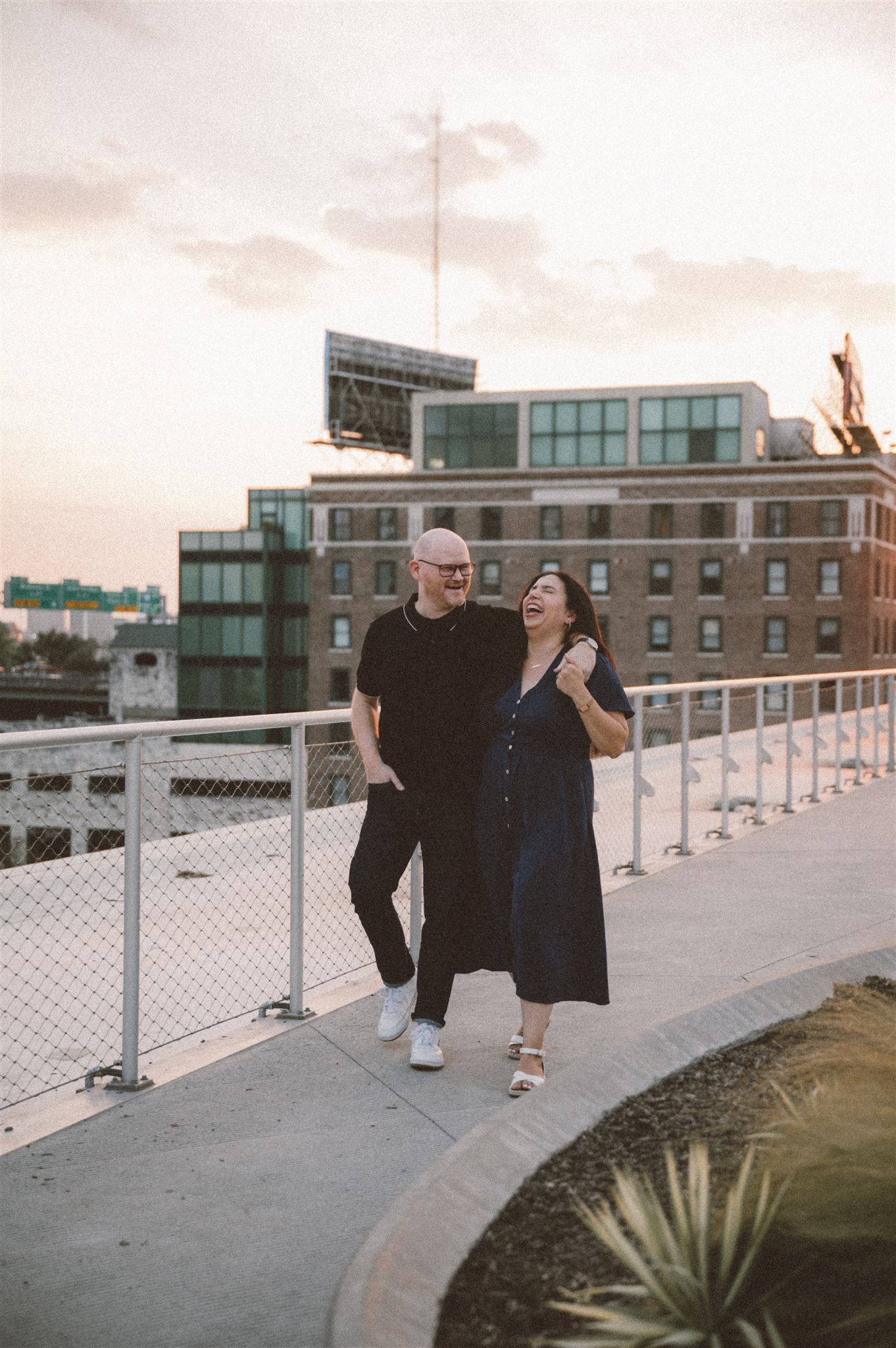 A couple poses together on a rooftop terrace with urban architecture in the background.