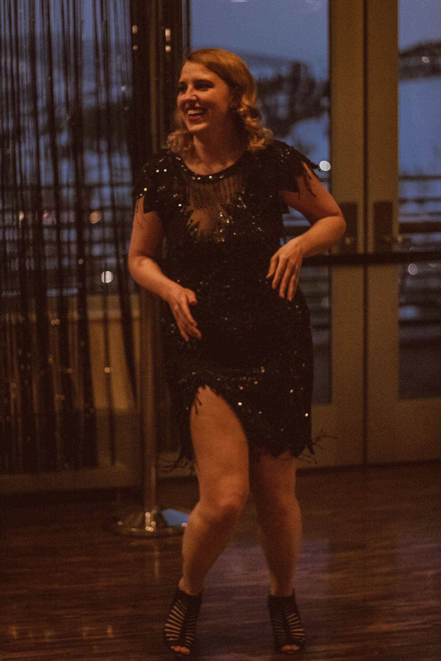 Dancer in sparkly black dress performs on wooden floor at twilight.