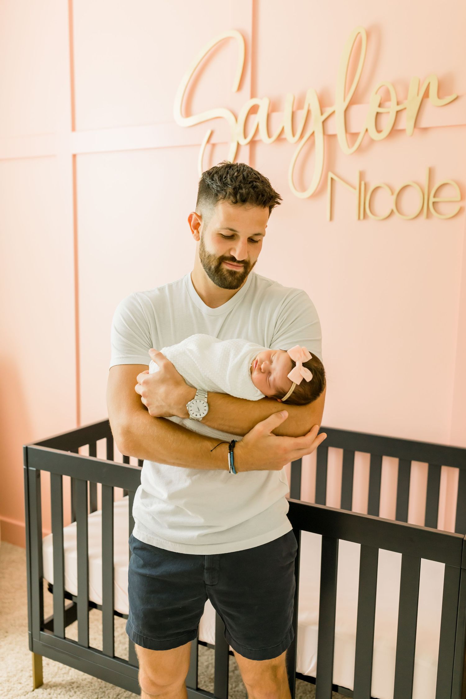 Adult holding sleeping newborn in modern coral nursery with name decor.