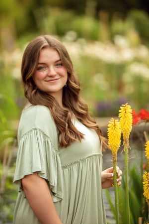 Someone in a sage green dress holds yellow flowers in a sunny garden setting.