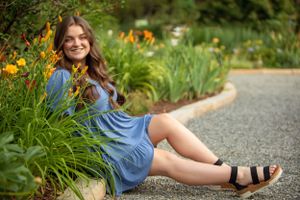 Person in blue dress sitting by flower garden path wearing sandals.