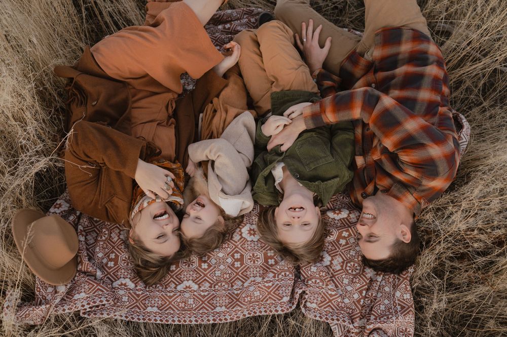 Small family of four sharing some laughs as they lay in a field and cuddle close together.