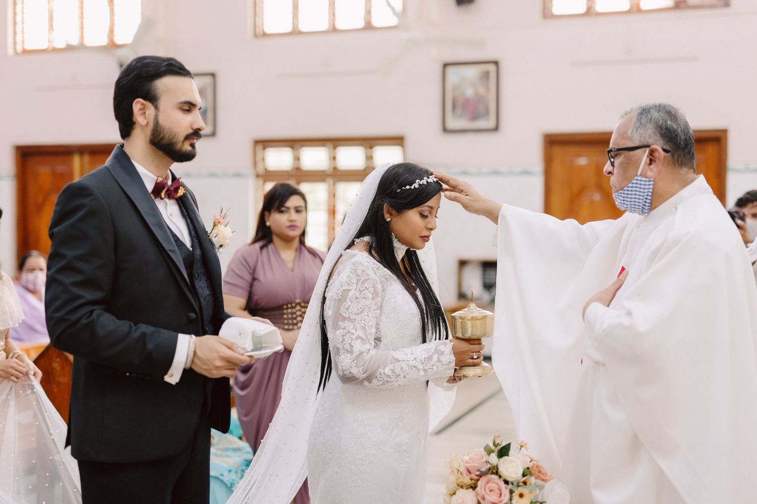 Traditional Catholic wedding ceremony taking place in a sunlit church sanctuary.