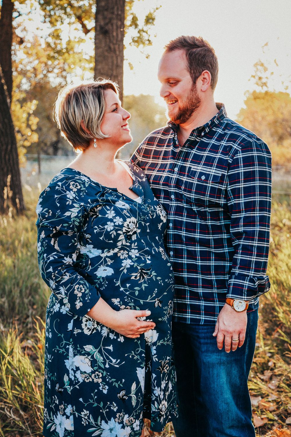 a pregnant woman smiles lovingly at her husband while touching her belly in a Denver field