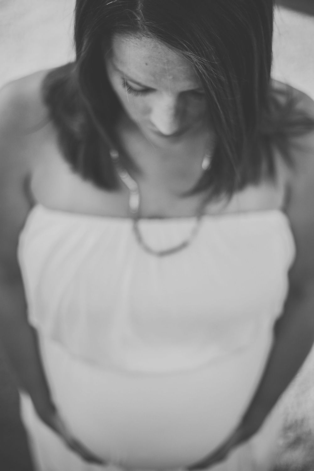 A pregnant mother looks down and cradles her belly in black and white maternity picture