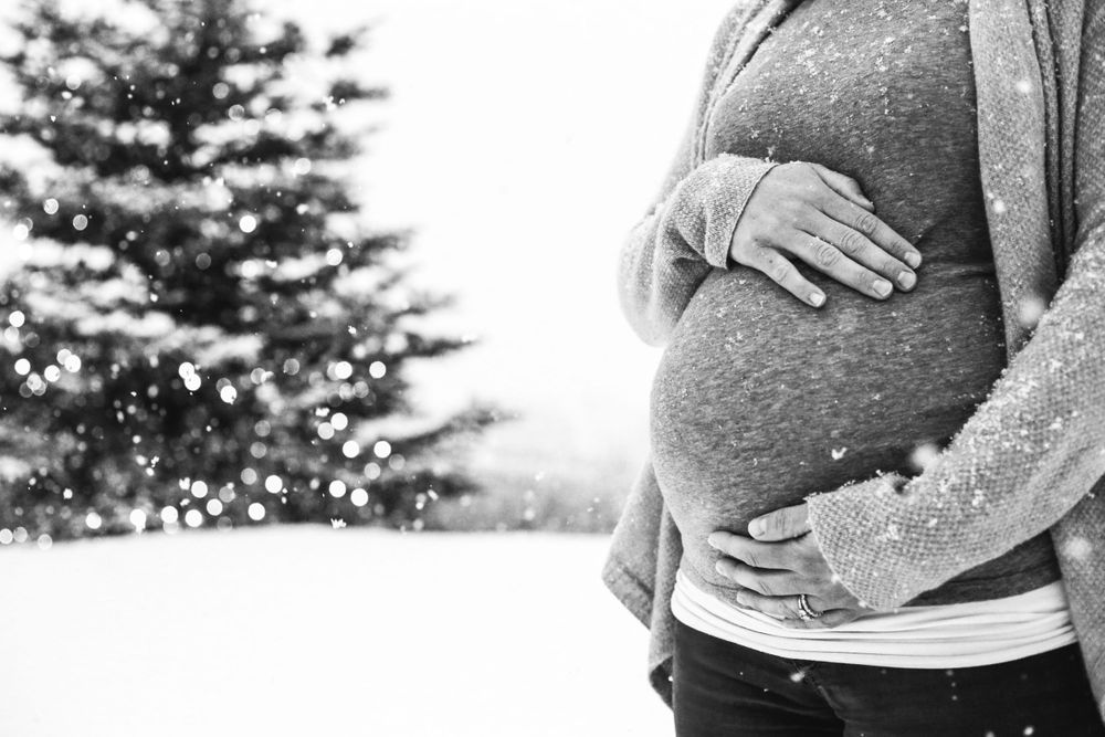 A pregnant mother cradles her belly in black and white maternity picture in the snow