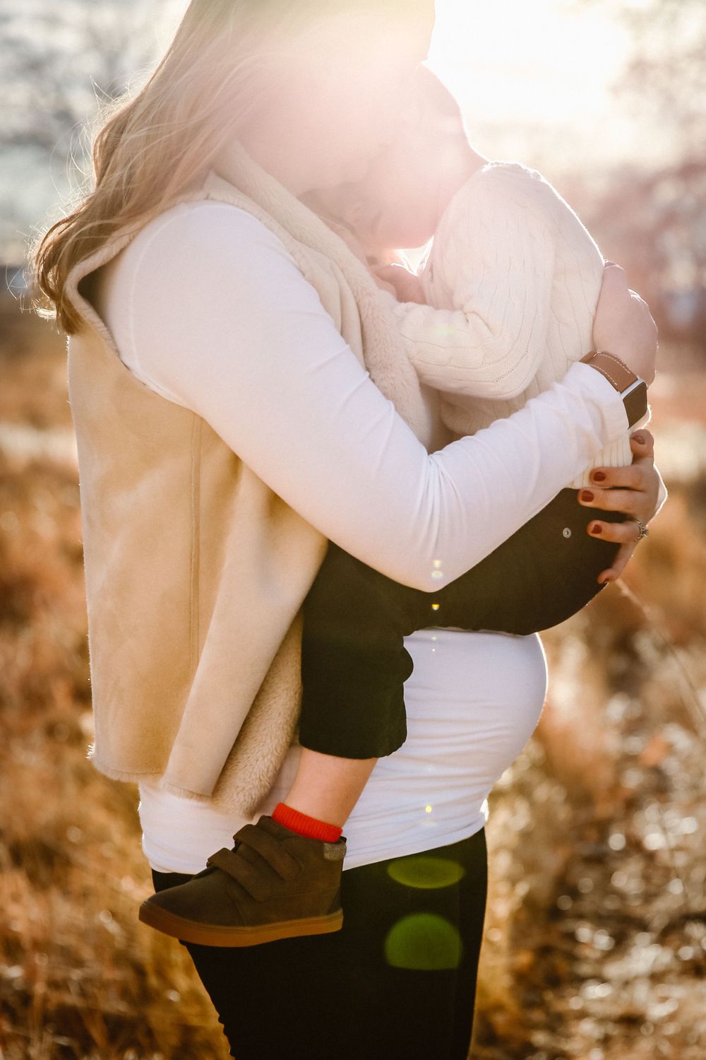 A pregnant mother holds her young child illuminated by golden hour sunlight