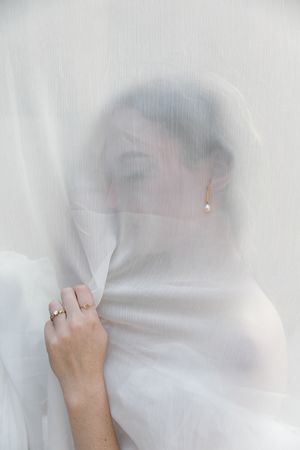 Details of pearl earrings shown through a veil.