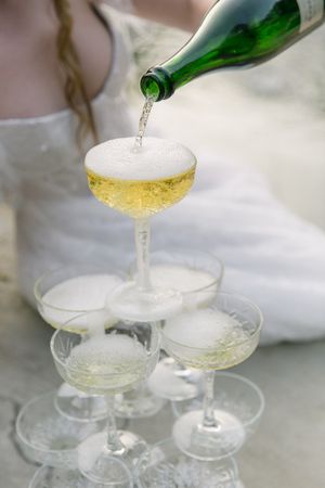 A champagne tower overflowing as champagne is poured from the top. A bride just visible in the background.