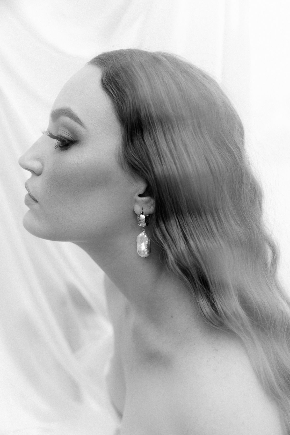 Side view of a long haired woman wearing pearl earrings.