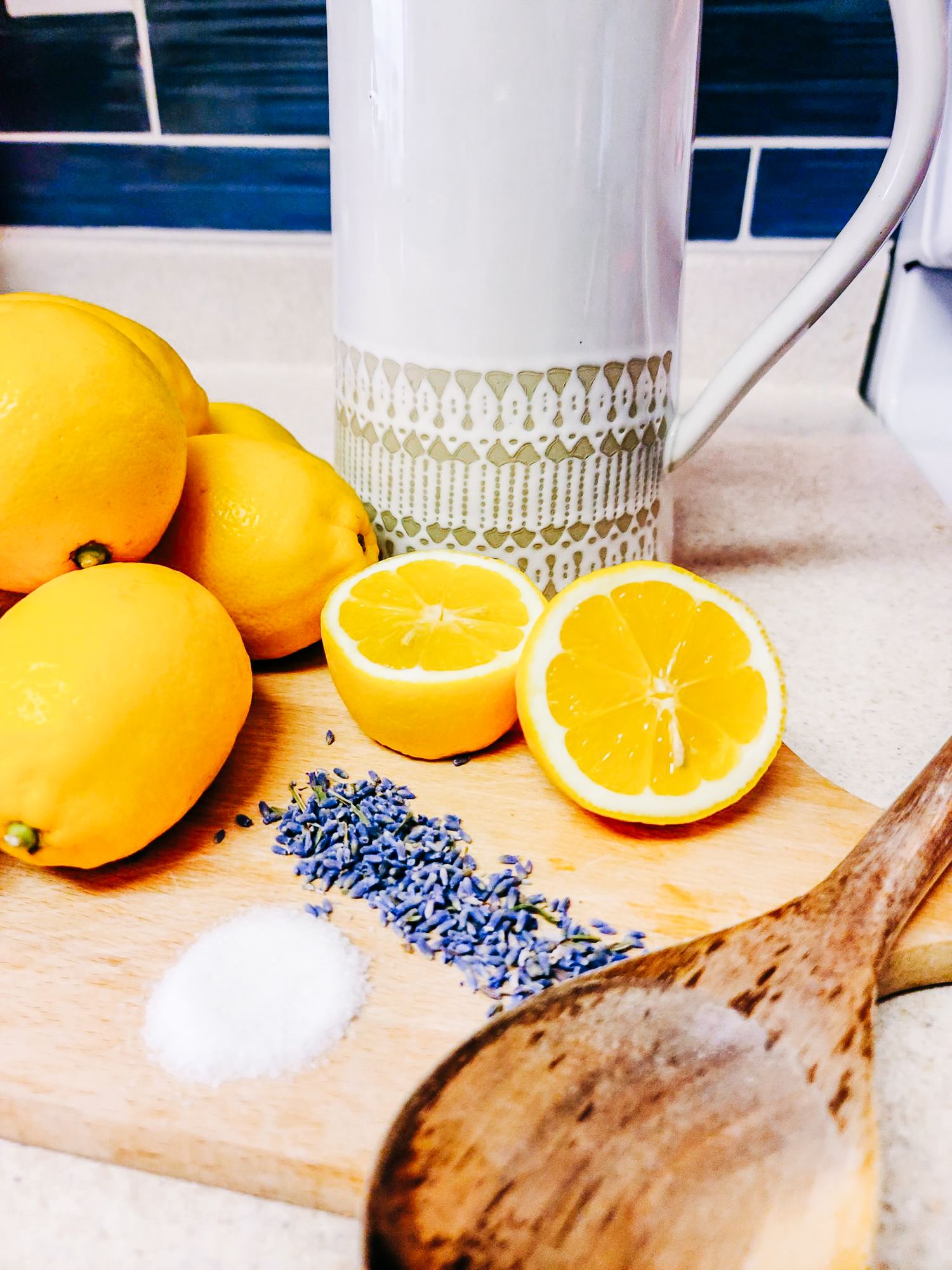 Fresh citrus and dried lavender displayed with a white pitcher on a wooden board.