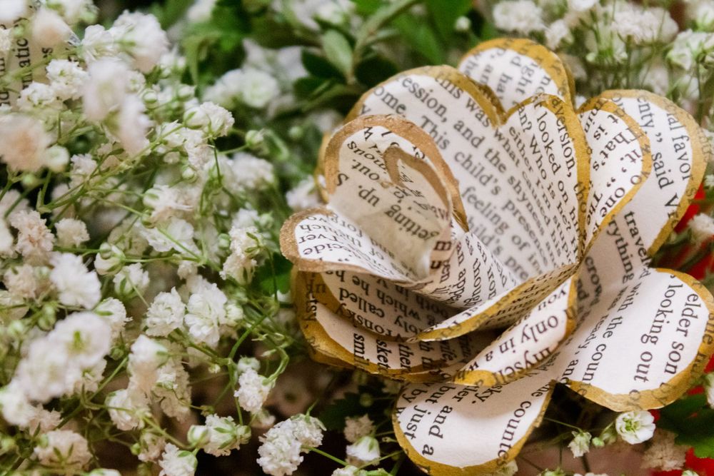 Paper rose made from book pages nestled among white baby's breath flowers.