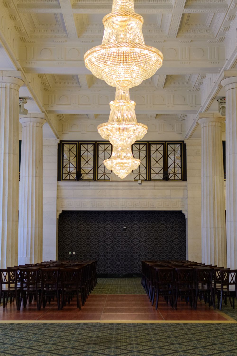 Elegant ballroom with crystal chandeliers, wooden chairs, and ornate columns in a neoclassical style.