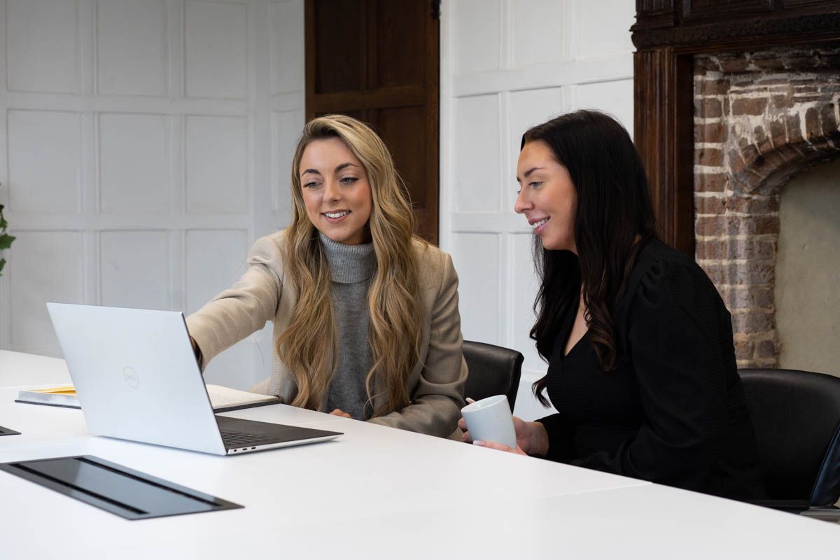 Two colleagues collaborating and sharing laptop screen in modern office setting.