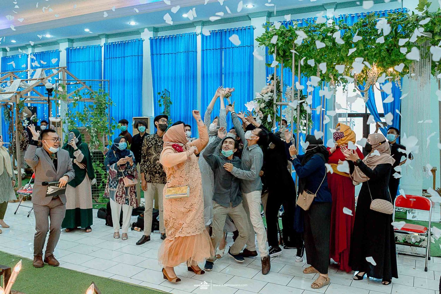 Wedding guests celebrating with joyful dancing and confetti in a blue-themed reception hall.