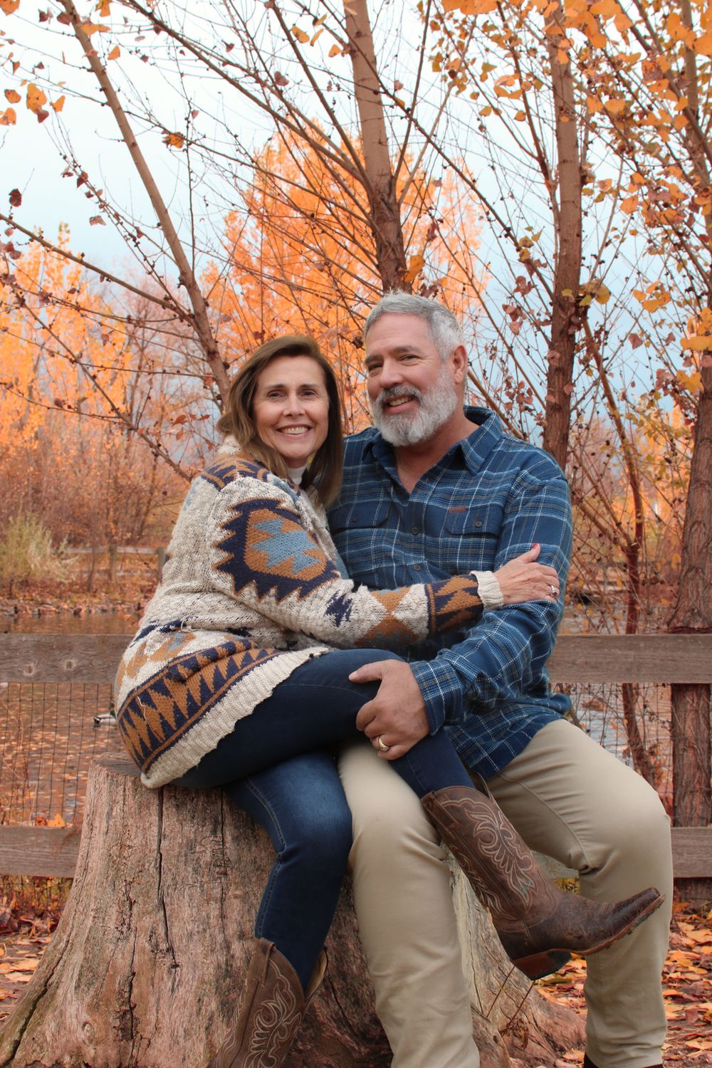 Couple sharing intimate moment while sitting on large tree stump in autumn setting.