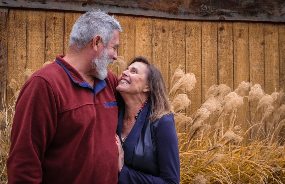 Intimate moment between couple against rustic wooden wall and ornamental grasses.